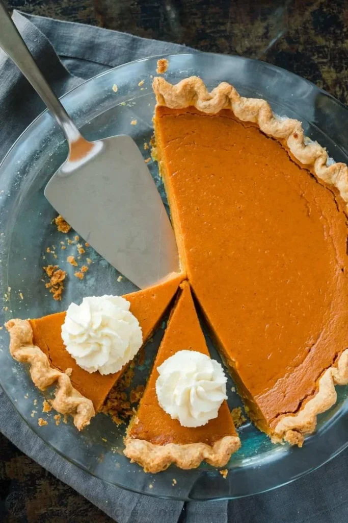 Classic pumpkin pie with whipped cream and spices on a wooden table