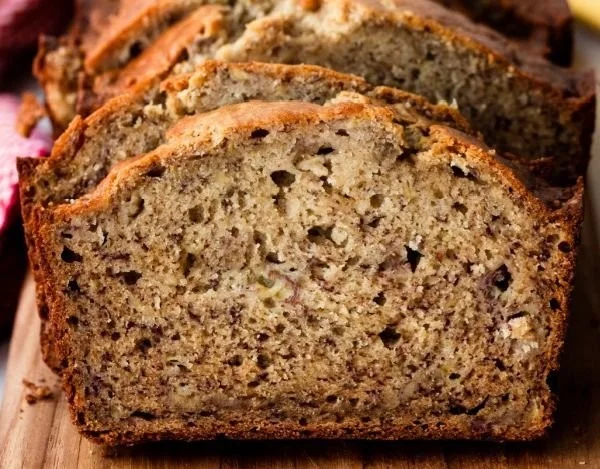 Slice of moist banana bread with a golden crust and ripe bananas